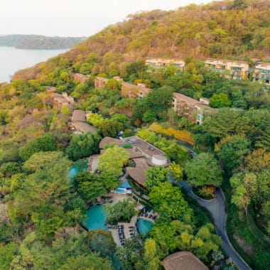 Aerial view of a lush resort nestled among green trees on a hillside overlooking a lake.