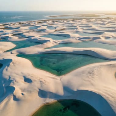Luftaufnahme der Lençóis Maranhenses in Brasilien mit weißen Dünen und türkisen Süßwasserlagunen im goldenen Abendlicht