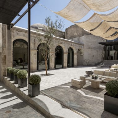 An outdoor lounge area with modern seating, potted plants, and shaded canopy in a spacious courtyard.