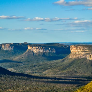 A panoramic view of the cliffs and canyon in the Chapada Diamantina, Brazil, with a partly cloudy sky overhead.