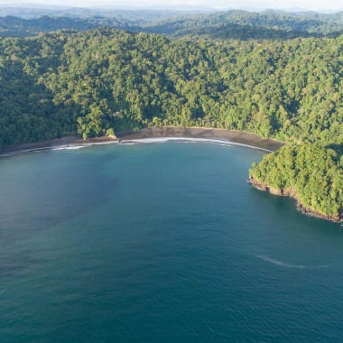 A panoramic aerial view of Morromico beach surrounded by dense green forest and clear blue ocean water.