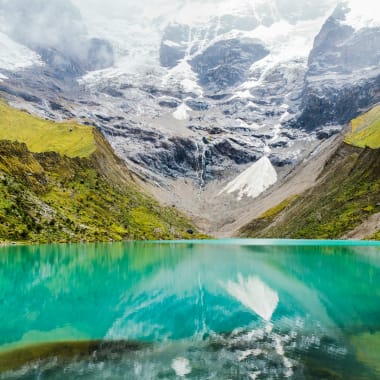 Türkisfarbener Humantay-See, der grüne Hügel und schneebedeckte Berge in Cusco, Peru, reflektiert.