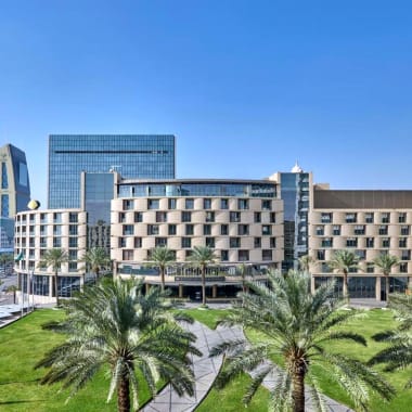 Moderne Hotelgebäude mit Palmen im Vordergrund, vor klarem blauen Himmel in Riyadh.