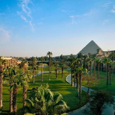 Üppiger grüner Garten im Marriott Mena House Cairo Resort mit Wegen und Palmen unter blauem Himmel.