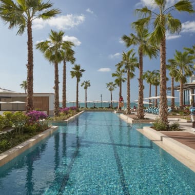 Ein luxuriöser Pool in einem modernen Hotel in Dubai mit Palmen und Strandblick.