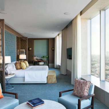 Luxury hotel suite with large windows offering a city view, modern furniture, and elegant decor.