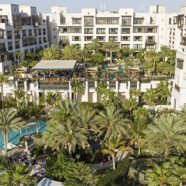 A luxurious residential complex with a central swimming pool surrounded by palm trees and modern white apartment buildings.