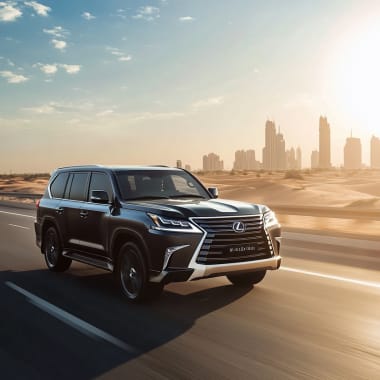 Ein schwarzer Lexus SUV fährt auf einer Autobahn mit Blick auf die Dubai-Hauptstadt im Hintergrund bei Sonnenuntergang.