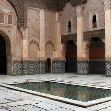 An inner courtyard of a traditional Moroccan building with intricate architectural details and a central fountain.