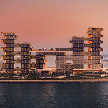 Modernes Atlantis The Royal Hotel mit gestaffeltem architektonischem Design am Wasser bei Sonnenuntergang, mit markanten gestapelten Blockstrukturen, die durch eine Hängebrücke verbunden sind.