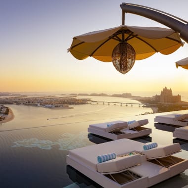 Luxuriöse Outdoor-Poolarea mit Liegen und Sonnenschirmen, Blick auf Fluss und Stadt bei Sonnenuntergang.