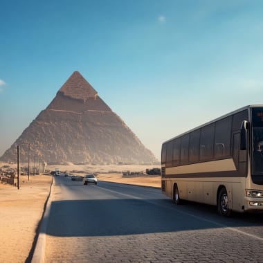 A coach bus driving on a road with pyramids in the background in Egypt.