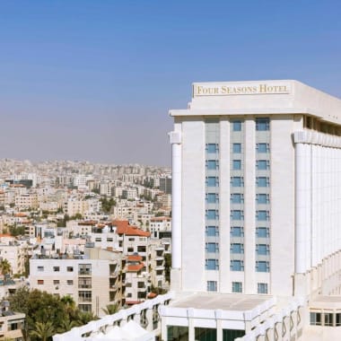 Ein hohes, weißes Four Seasons Hotel Gebäude ragt in einer Stadtlandschaft mit vielen kleineren Gebäuden im Hintergrund während des Tages auf.