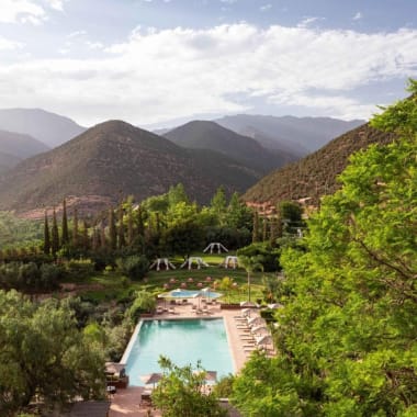 Eine malerische Landschaft mit einem Pool, umgeben von üppigem Grün und Bergen im Hintergrund.