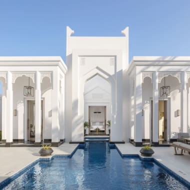 Ein eleganter weißer Palast mit islamischen Architekturelementen, mit einem zentralen Brunnen und einem reflektierenden Pool im Vorderhof.