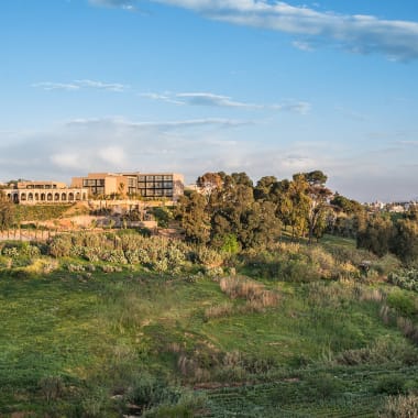 Außenansicht des Hotel Sahrai mit moderner Architektur, umgeben von grüner Vegetation unter teilweise bewölktem Himmel.