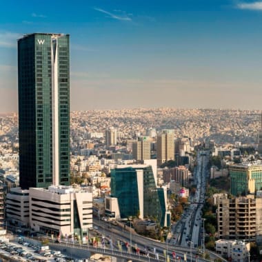 Stadtbild von Amman mit hohen modernen Gebäuden und Autobahnen unter einem blauen Himmel.