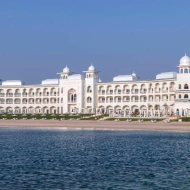Das Chedi Katara Hotel und Resort, ein großes weißes Gebäude mit Kuppeltürmen, am Wasser gelegen.