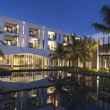 Luxurious hotel resort with modern architecture, surrounded by palm trees, reflecting in a calm pool at night.