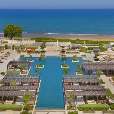 A luxurious beach resort with a large swimming pool, surrounded by lounge chairs and cabanas, overlooking the ocean.