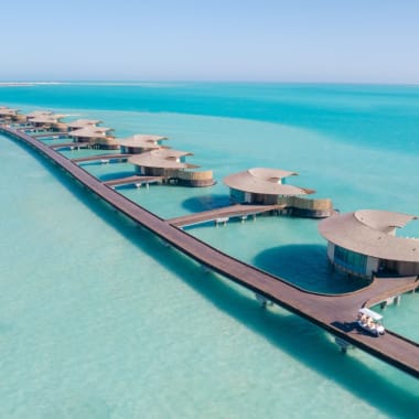 Luftaufnahme von Wasserbungalows, die durch einen Steg an einem Resort am Roten Meer verbunden sind, mit türkisfarbenem Wasser.