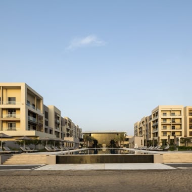 Modern hotel complex with symmetrical white buildings, a central water feature, and a clear blue sky.