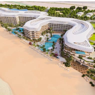 A luxury resort with modern, curvy white buildings along a sandy beach, featuring pools and palm trees.