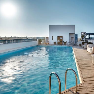 Dachpool auf einer Hotelterrasse mit weißen Sitzbereichen und Stadtblick im Hintergrund unter einem sonnigen Himmel.