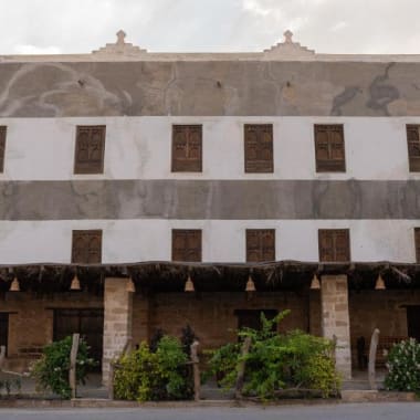 The exterior of Koofan Heritage Lodge, a traditional multi-story building with wooden window shutters and a small garden in front.