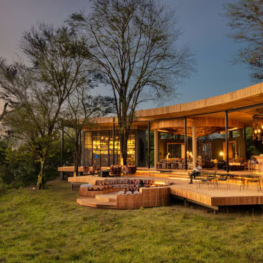 Luxus-Gästebereich mit offene hölzerne Terrasse, die auf eine grüne Landschaft mit Bäumen bei Sonnenuntergang blickt.