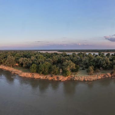 Eine Panoramasicht auf einen Fluss, der auf ein sattes, bewaldetes Land trifft, bei Sonnenuntergang.
