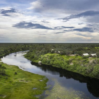 An aerial view of a winding river flowing through lush green landscape in Botswana under a cloudy sky.