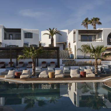 Luxuriöse weiße mediterrane Gebäude mit Balkonen und Palmen, die einen einladenden Swimmingpool mit gepolsterten Sitzgelegenheiten auf dem Deck am Tag umgeben.