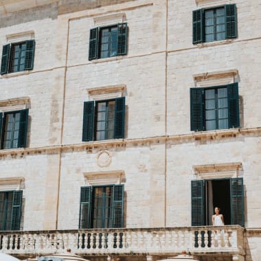 A historic hotel building with multiple windows and shutters in Dubrovnik, Croatia, with a person standing on a balcony.