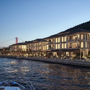 Luxuriöse Gebäude entlang des Bosporus mit einer Brücke im Hintergrund bei Dämmerung.