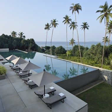 Luxuriöser Infinity-Pool mit Blick auf eine tropische Landschaft mit hohen Palmen und den Ozean im Hintergrund.