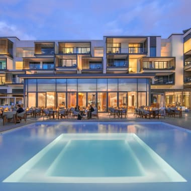 Elegantes Hotel oder Resort mit beleuchtetem Schwimmbad und Außenterrasse bei Dämmerung.