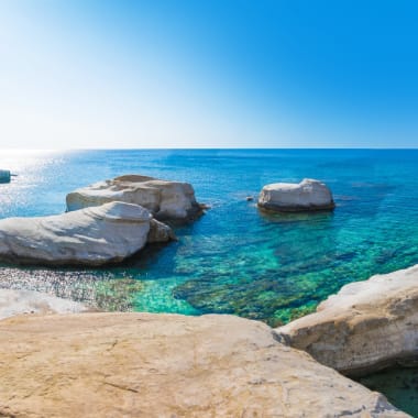 Eine Panoramaaufnahme der Küste von Paphos in Zypern mit klarem, blauem Wasser und felsigem Ufer.