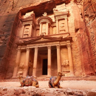The ancient rock-cut city of Petra in Jordan features a spectacular facade carved into the rose-red cliffs with camels in the foreground.