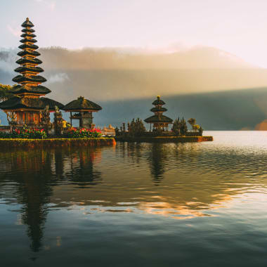 Sonnenuntergang über dem Ulun Danu-Tempel am See Bratan in Bali, Indonesien, mit Bergen, die sich im Wasser spiegeln.