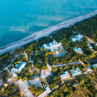 Luftaufnahme eines Küstenbereichs in Mosambik mit Gebäuden, umgeben von Grünland und einer Strandküste.