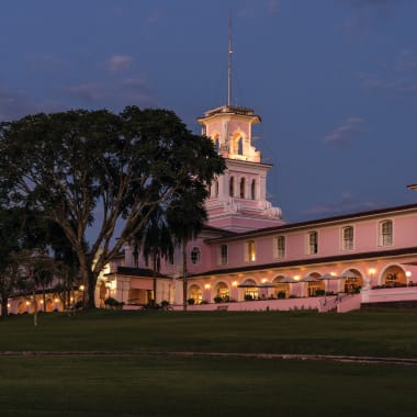 The exterior of the Belmond Hotel in Brazil illuminated at dusk with a large tree nearby.