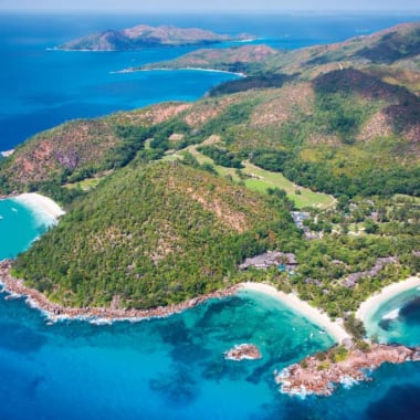 Aerial view of Constance Lemuria resort surrounded by lush greenery, turquoise waters, and sandy beaches on a tropical island.