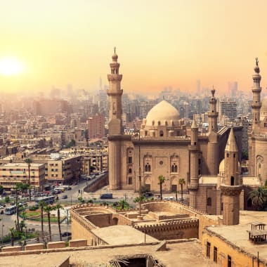 Sunset over Cairo skyline with historic mosques and modern buildings.