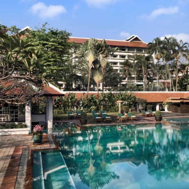 A luxurious hotel pool area surrounded by palm trees and lounge chairs under a clear blue sky.
