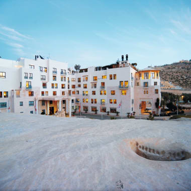 Das Moevenpick Resort Petra mit moderner weißer Architektur vor einem Hügel unter blauem Himmel.