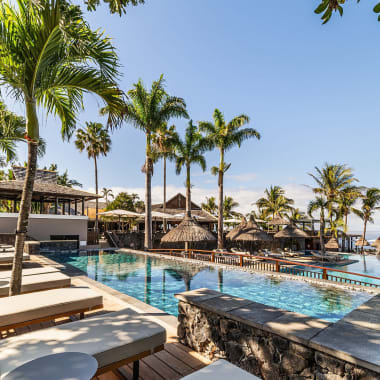 Außenpool-Bereich eines tropischen Hotels oder Spas mit Liegestühlen, Palmen und klarem blauem Himmel am Meer.