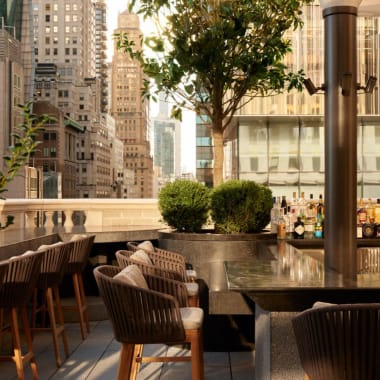 Eine Dachterrasse im Freien in New York City mit Sitzgelegenheiten, Pflanzen und Stadtgebäuden im Hintergrund.