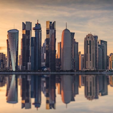 Eine Stadt-Skyline bei Sonnenuntergang, die sich auf Wasser spiegelt, mit hohen modernen Gebäuden.