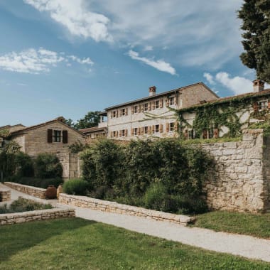 Ein malerischer Blick auf das Meneghetti Wine Hotel mit historischen Steingebäuden und sattem Grün in Bale, Kroatien.